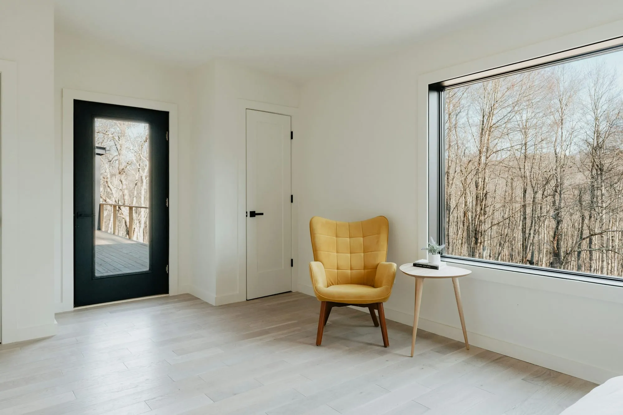 Heller weißer Raum mit gelbem Sessel am Fenster, draußen Bäume
